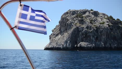 flag of greece flying in the wind on boat on sea with cliffs in background