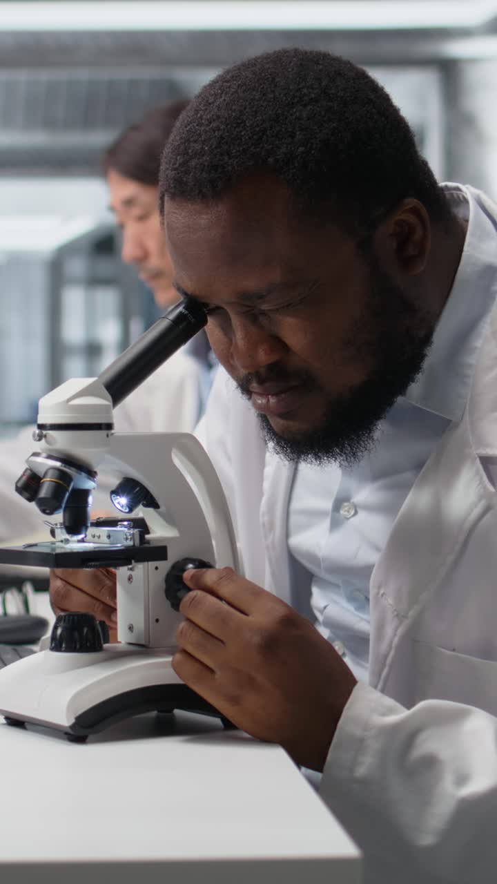 Video verticale: microbiologo clinico in laboratorio che usa il microscopio per la ricerca in patologia