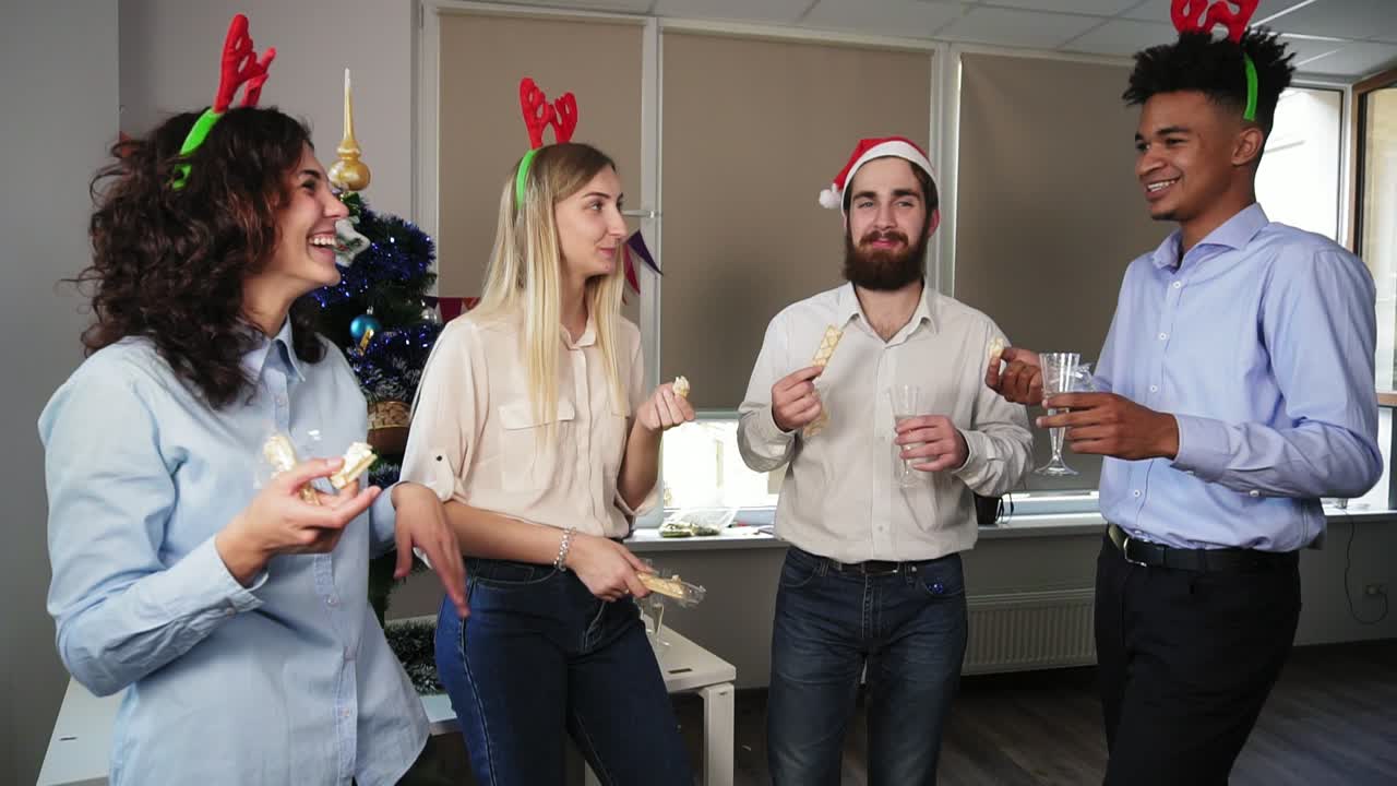 Multiracial group of happy office workers holding glasses with sparkling wine and talking taking snacks during christmas party