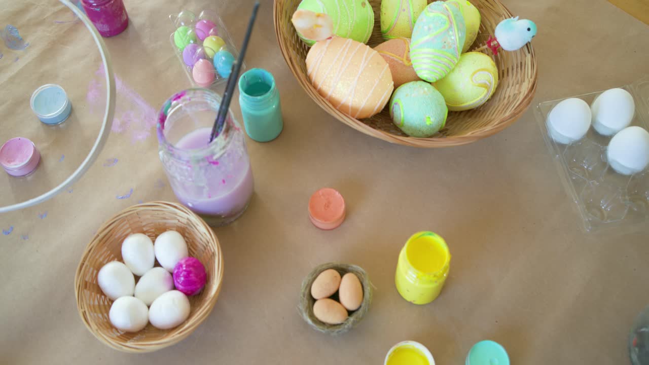 Camera is panning down and right, revealing paint pots, brushes, and pastel eggs to showcase setup