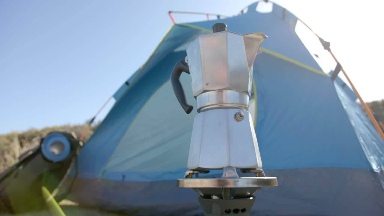 Camping with moka pot, making coffee in front of blue tent in mountains