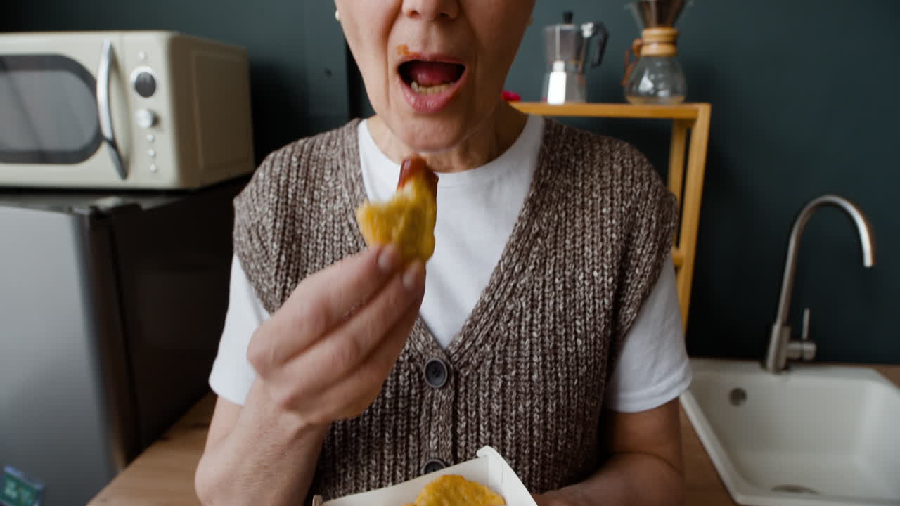 Close-up of a woman eating chicken nuggets in a kitchen
