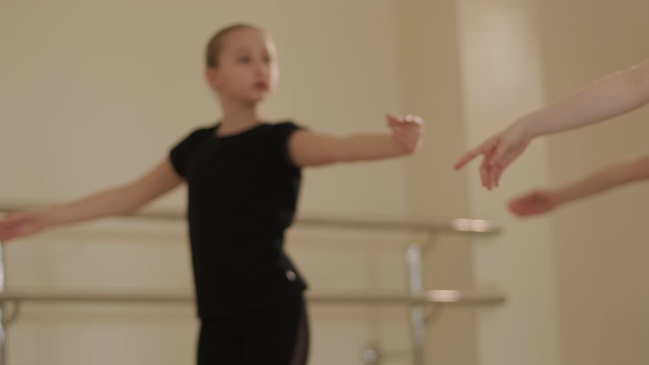 A group of young ballet students in black dancewear practicing positions in a spacious ballet studio with wooden flooring and wall-mounted barres. Focused expressions and synchronized movements.