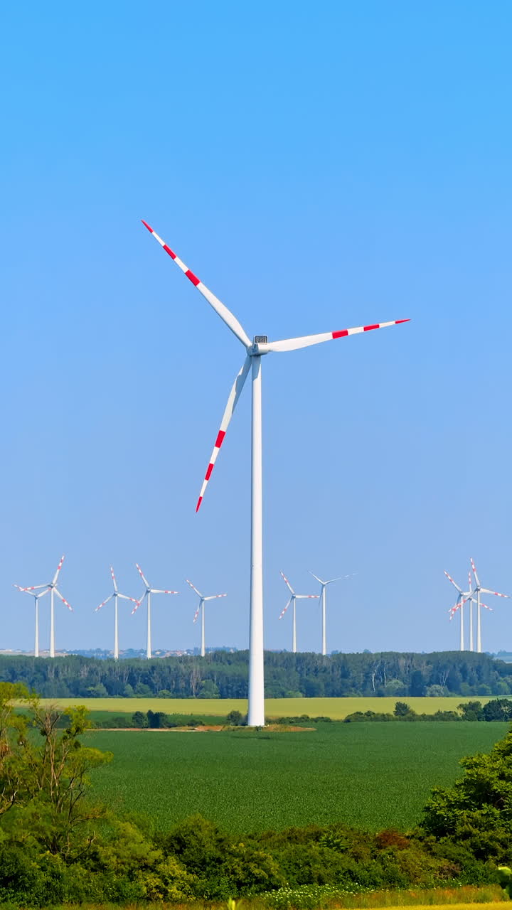 Wind turbines in a field. A large wind turbine stands prominently in a green field with several others in the background under a clear blue sky