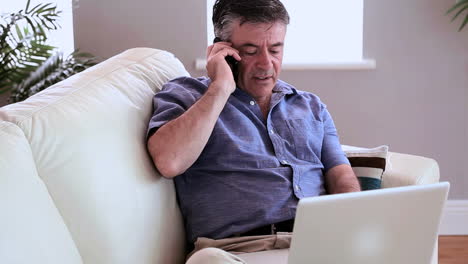 annoyed man talking on the phone on the sofa with his laptop