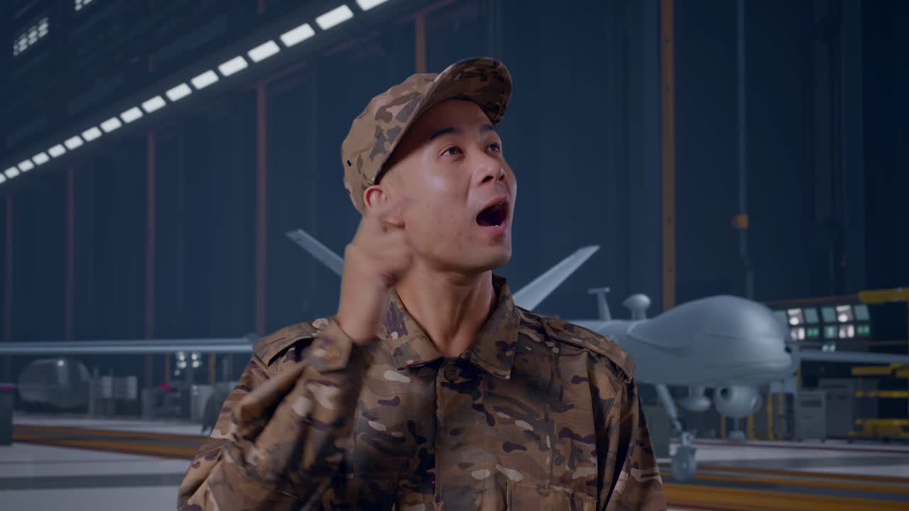 Close Up Of Asian Man Soldier Thinking And Looking Around Then Raising His Index Finger While Standing With Modern Military Drone In Maintenance Hangar