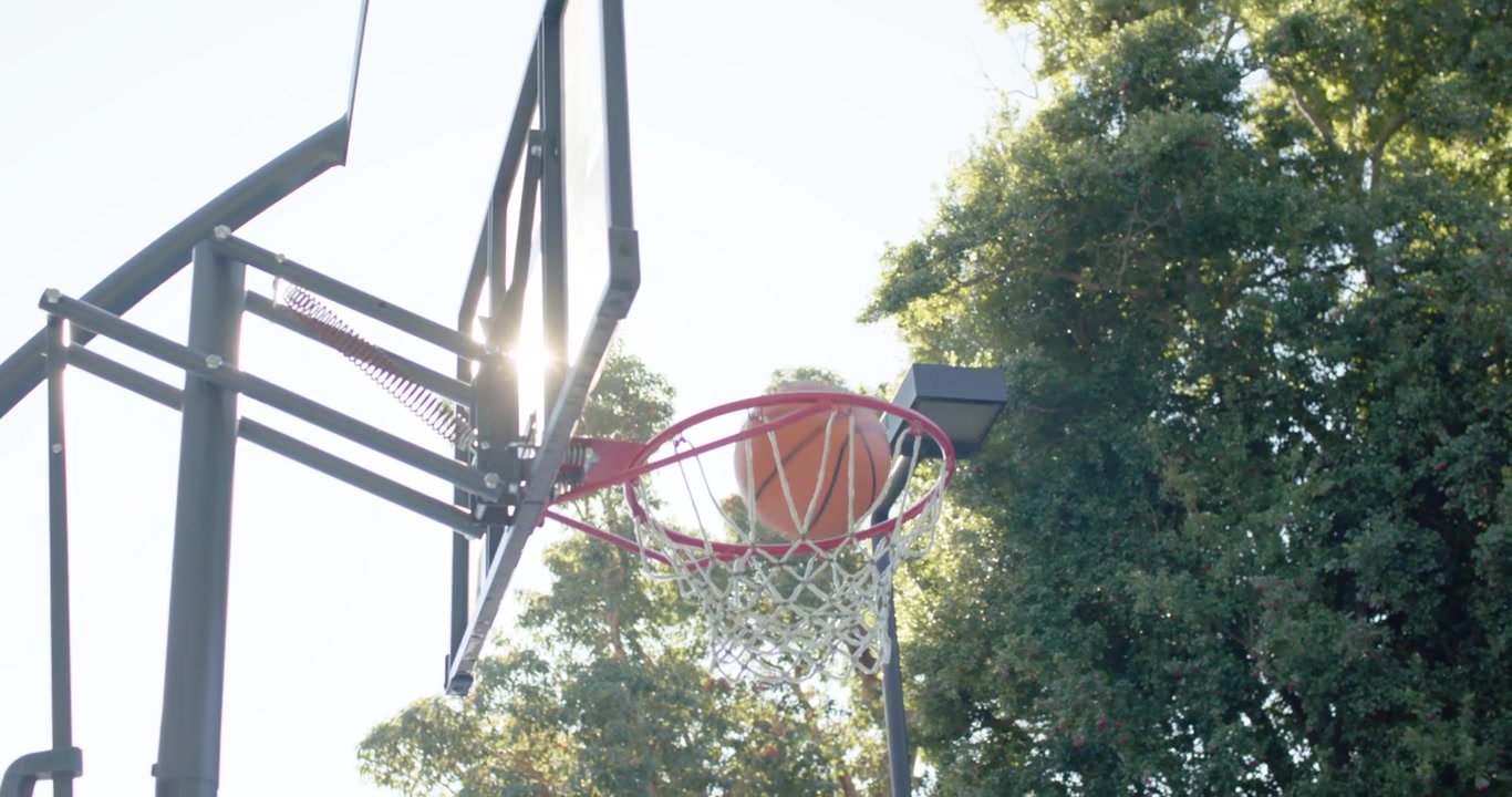 Män med olika bakgrund spelar på en bakgårdsplan, en man i hoodie kastar basketboll, en afroamerikansk man skjuter lay-up