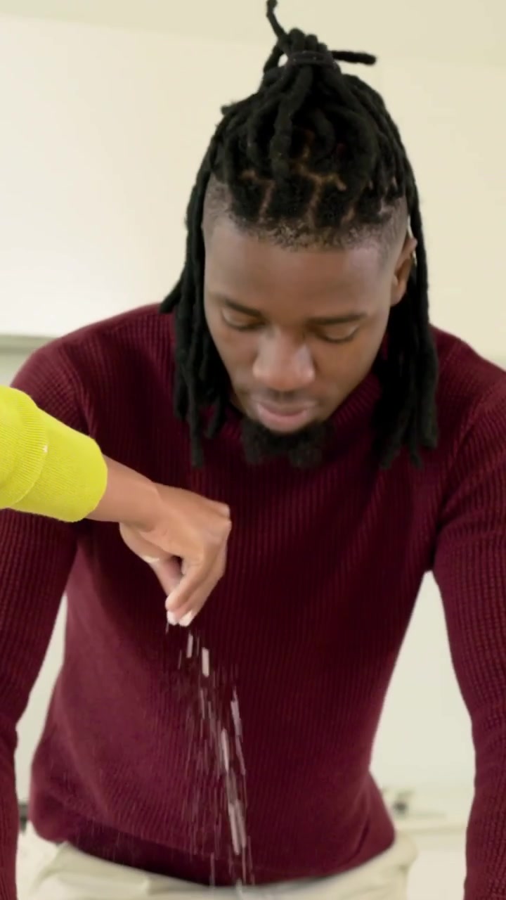 Video vertical: Hombre reaccionando, vestido de granate, amasando en la cocina mientras su pareja, de amarillo, añade harina y cocina.