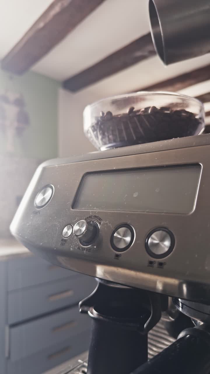 Primo piano verticale di chicchi di caffè tostati che cadono nella tramoggia di una macchina da caffè espresso domestica all'interno di un ambiente cucina