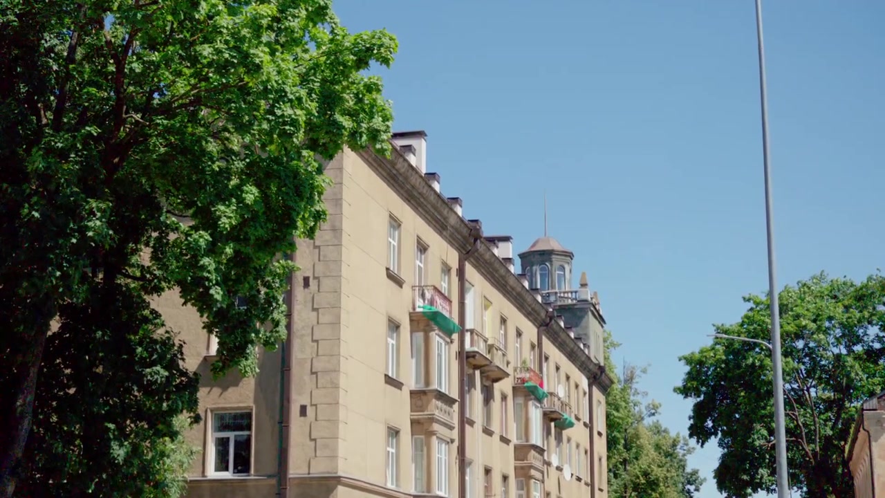 Vista panoramica dal basso della facciata di un edificio architettonico classico stalinista giallo con torre angolare decorativa e alberi verdi a Daugavpils, Lettonia, sotto un cielo azzurro brillante