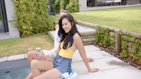 a young caucasian girlfriend is seated by a pool in the backyard at home, smiling broadly