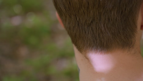 back view of white man showing ear and shaved side beard skin while untying headband, highlighting neck tattoo and detailed grooming, in natural outdoor environment with soft sunlight