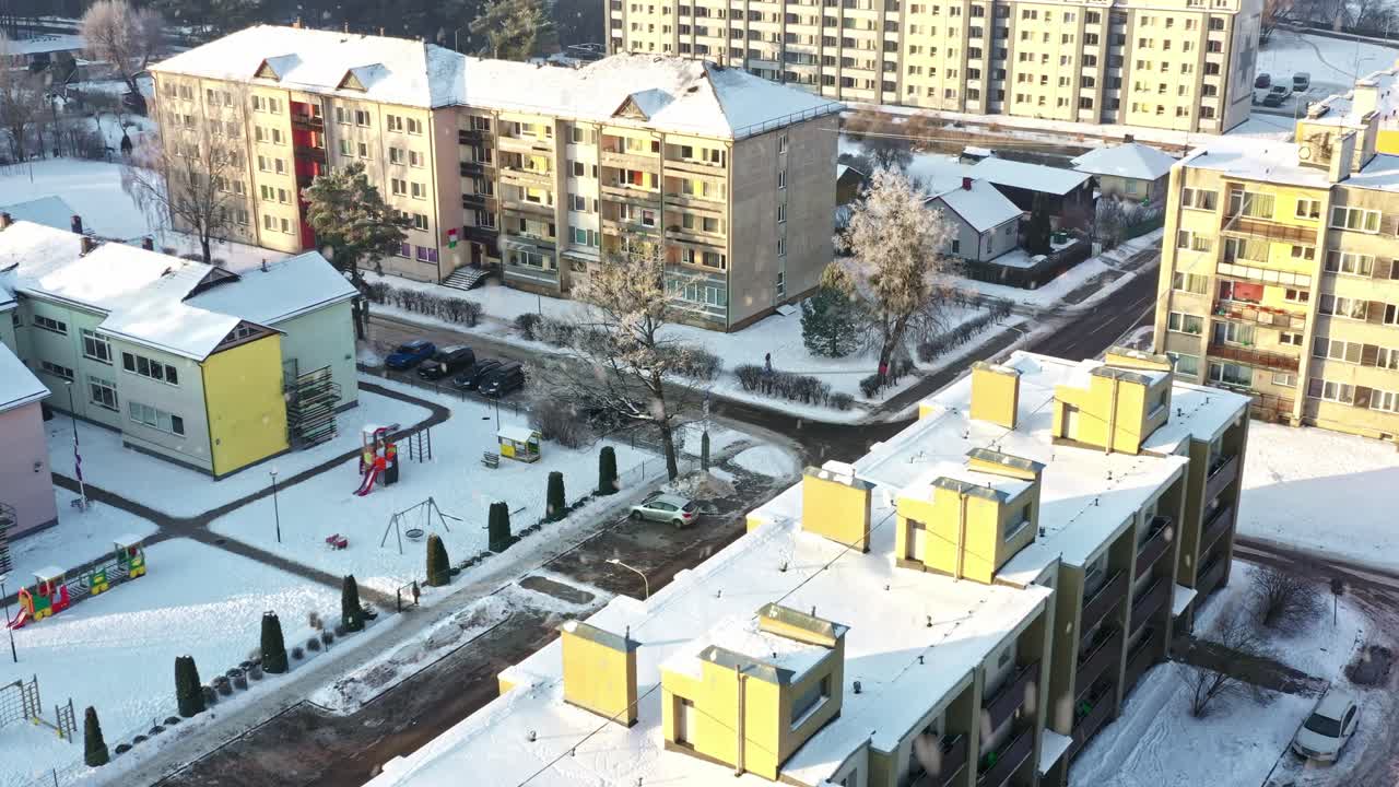 Area residenziale coperta da neve invernale, condomini e parchi giochi con nevicata in una soleggiata mattina d'inverno, ripresa dall'alto