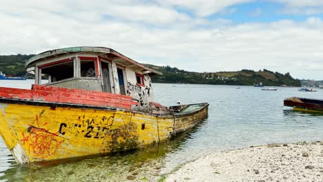 abandoned typical boat moored at dalcahue shoreline , pan shot