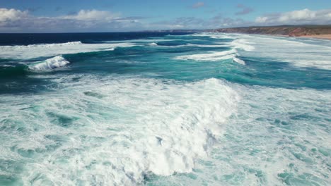 vuelo aéreo de drones 4k de una pareja disfrutando de una vista panorámica de la pintoresca playa con olas perfectas para surfear en la playa de arena de bordeira en la región del algarve de portugal