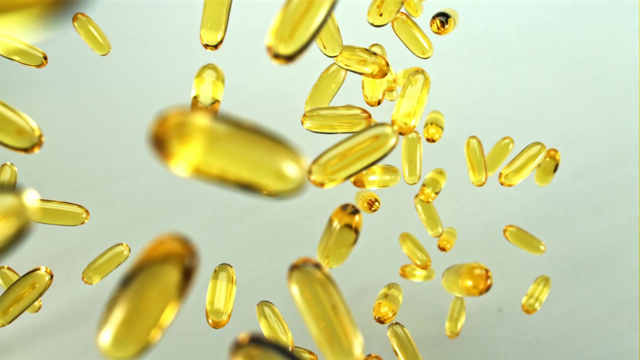 Capsule gialle di olio di pesce Omega-3 che cadono al rallentatore.