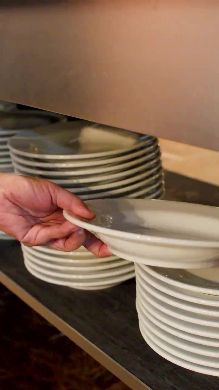 A hand reaches into a restaurant buffet line to pick up clean white ceramic plates