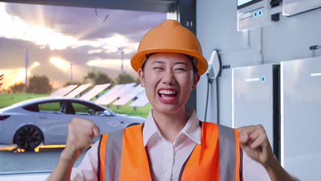 close up of asian female engineer with safety helmet screaming goal and dancing celebrating with home energy storage system in a modern garage