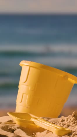 Vertical-Video-Summer-Holiday-Concept-With-Child's-Bucket-Spade-On-Sandy-Beach-Against-Evening-Sea-Background