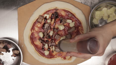 top static view on male hand spreading delicious barbeque sauce on meat pizza