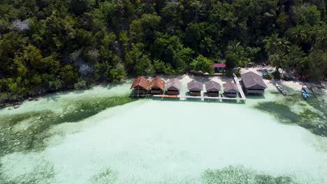 aerial pull out of exotic waterfront huts over crystal clear ocean water in raja ampat, west papua, indonesia