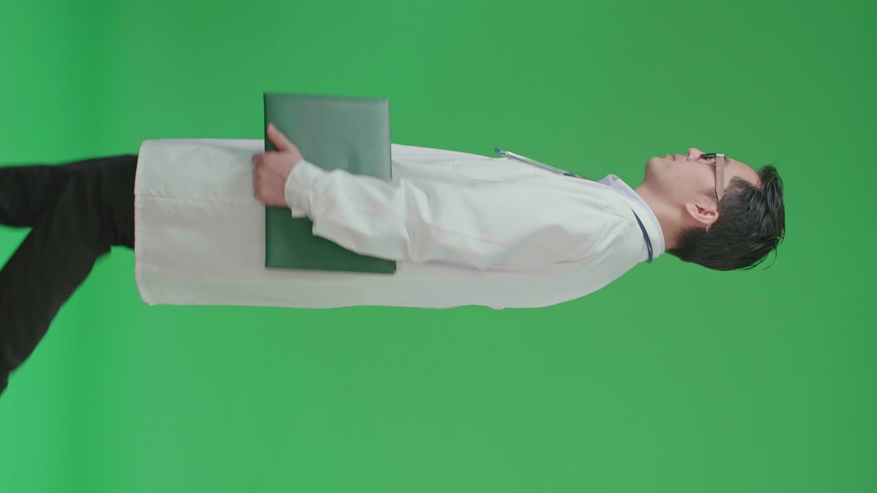 The Side View Of Asian Doctor With Stethoscope Wearing Glasses And White Coat Holding Document File While Walking On Green Screen Chroma Key.