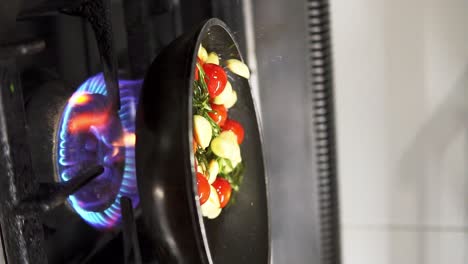 clip de cierre vertical de la persona revolviendo una sartén de verduras en la estufa de la cocina en cámara lenta