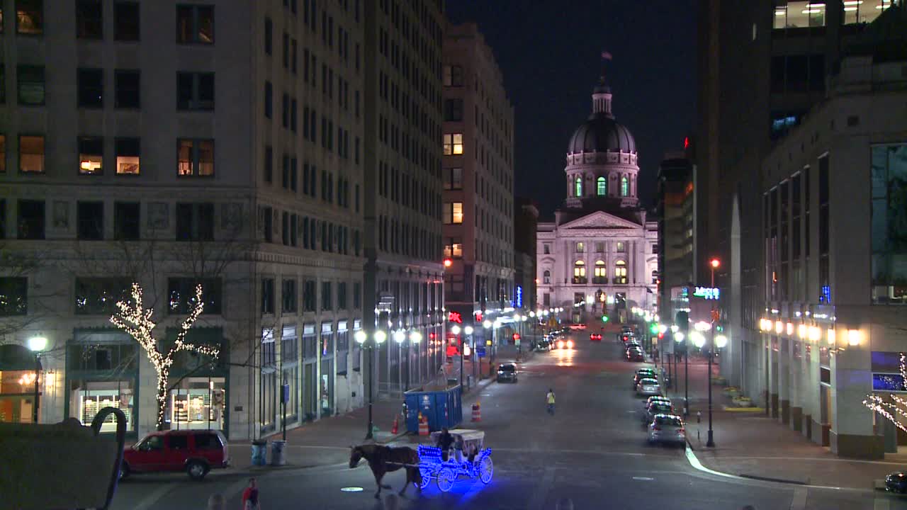 말이 끄는 마차가 밤에 인디애나폴리스에 있는 인디애나 주 수도 건물을 통과합니다.