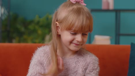 portrait of little adorable child girl sitting alone on sofa at home looking at camera and smiling