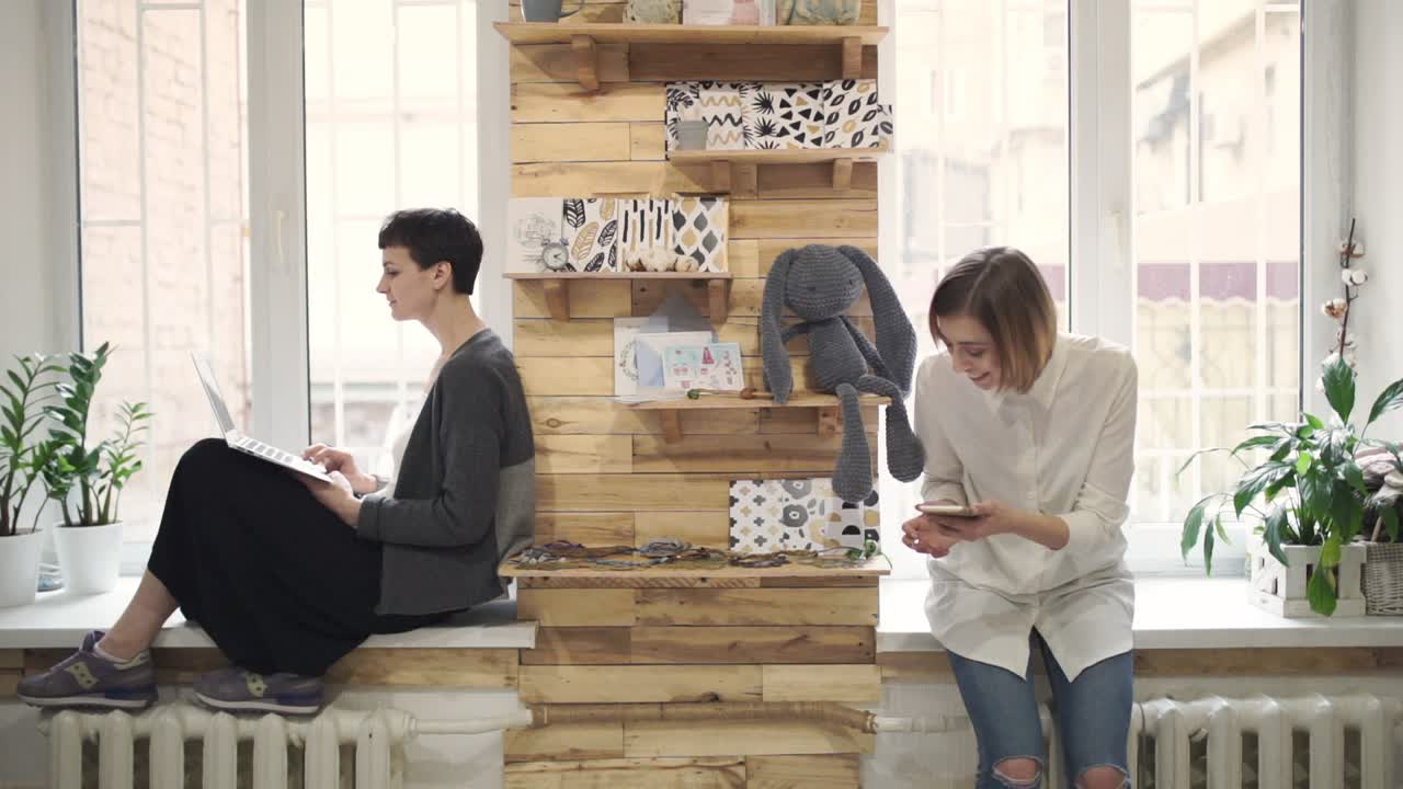 창 ⁇ 에 앉아서 노트북을 사용하는 젊은 여성. 스마트 폰을 사용하는 여성