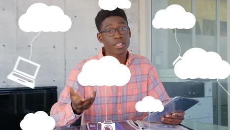 Animation of clouds and digital icons over businessman using tablet