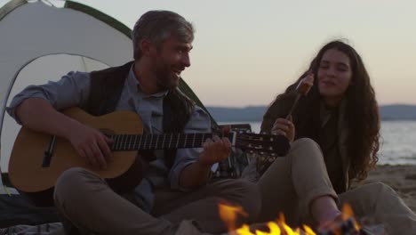 pareja alegre haciendo un picnic romántico en la playa por la noche