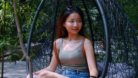 young asian girl sitting on hanging chair smiling while looking around the park brisbane, australia