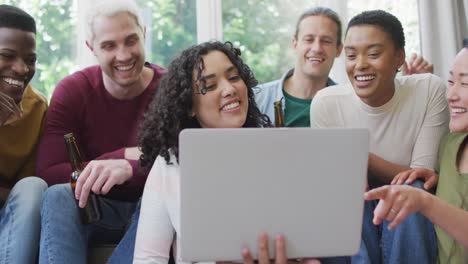 grupo diverso de amigos felices hombres y mujeres mirando la computadora portátil y riendo en la sala de estar