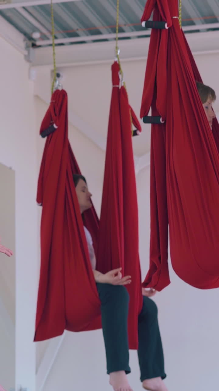 tired women sit relaxed after oriental fly yoga workout in special hammocks and practice breathing exercise