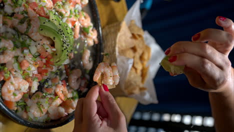 mouvement lent vertical d'une main féminine pressant un citron sur une puce de tortilla avec des crevettes d'un ceviche mexicain traditionnel avec de l'avocat