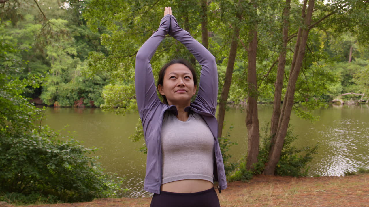 Woman Wearing Sports Clothing Doing Yoga Stretching In Forest By Lake Or River Enjoying Peace And Beauty Of Nature
