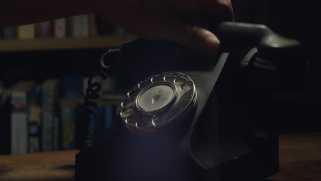 person puts handset down on 1950s black retro-style telephone after answering call at nighttime, close up shot