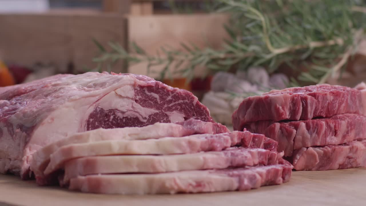 Primo piano di fettine di controfiletto di manzo marmorizzato fresco e crudo e medaglioni di bistecca su un tagliere di legno con rosmarino
