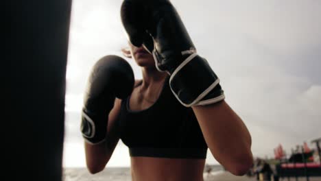 vista de cerca de una fuerte boxeadora atlética en guantes haciendo ejercicio con una bolsa. entrenamiento al aire libre. entrenamiento de boxeadora.