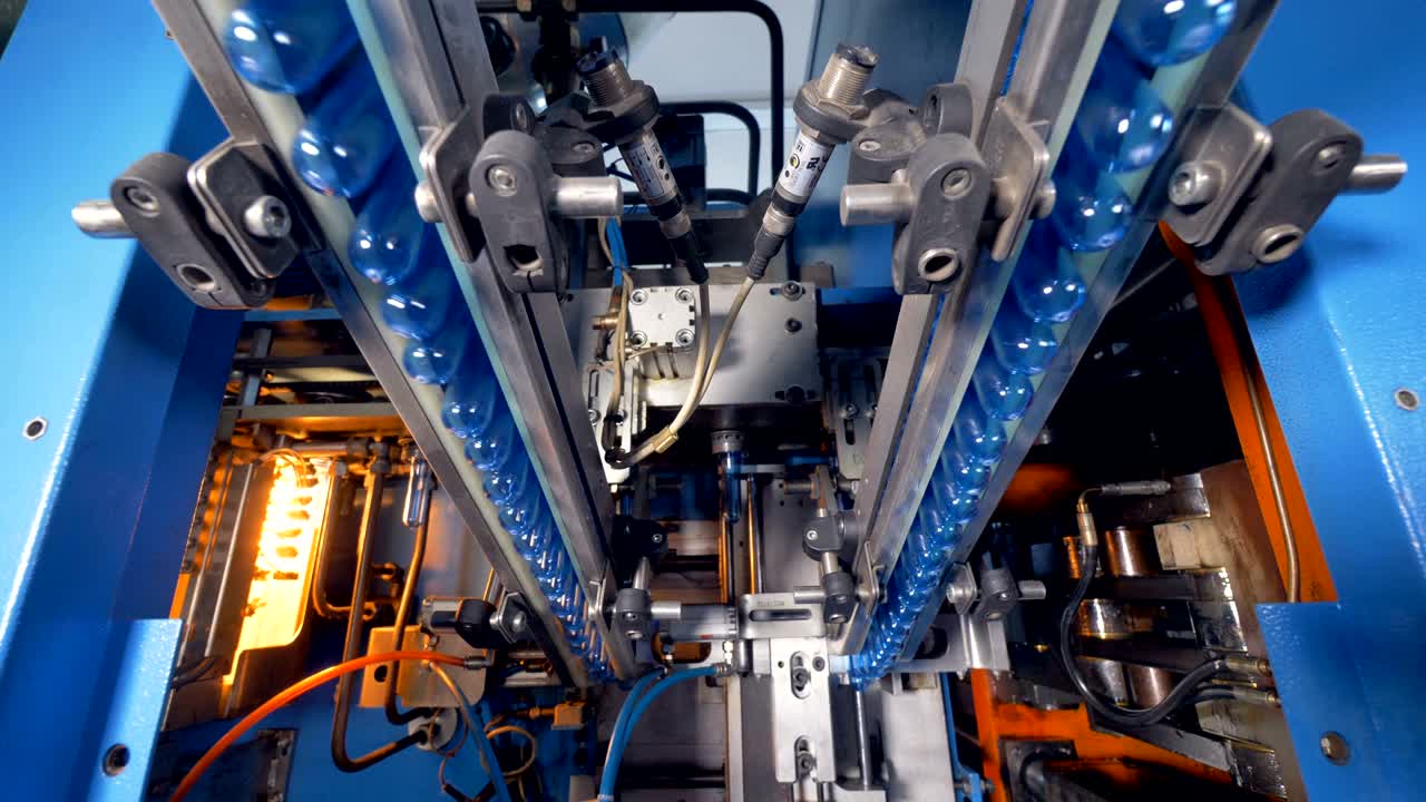 las preformas de botellas para mascotas se agarran y se elevan para entrar en la cámara de soplado.