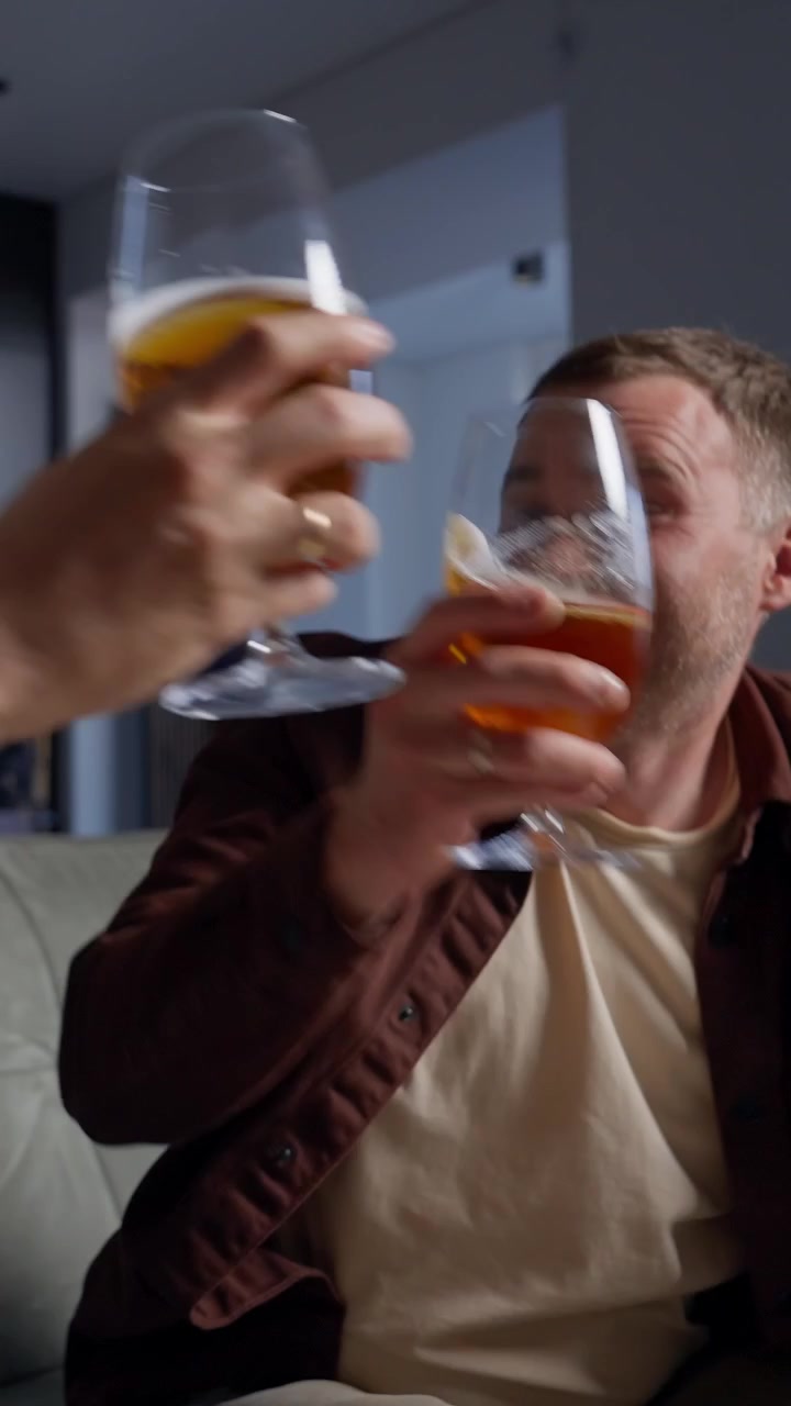 Excited Man Cheers and Toasts with Beer While Watching at Home