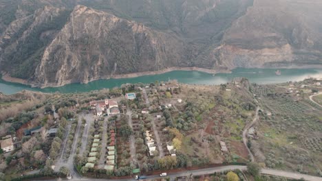 Top-view-of-Canales-Reservoir-with-vehicles-moving-on-the-road-and-big-mountain-behind-,-Spain