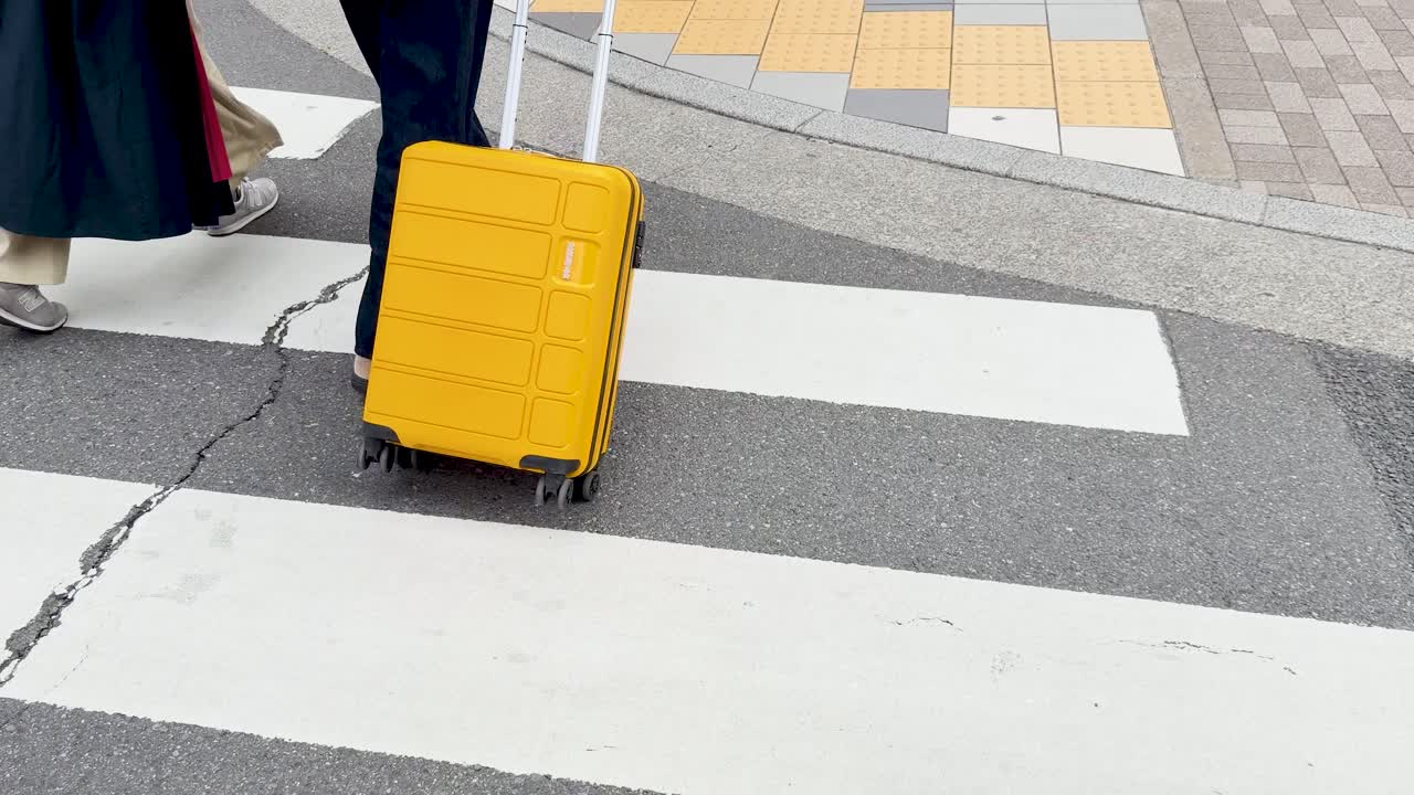 Một du khách kéo vali màu vàng qua vạch kẻ đường dành cho người đi bộ trên một con phố ở Tokyo