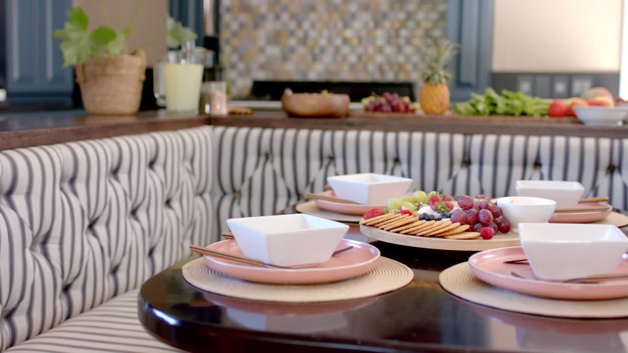 Dining table set with plates and bowls, serving fruit and cheese platter