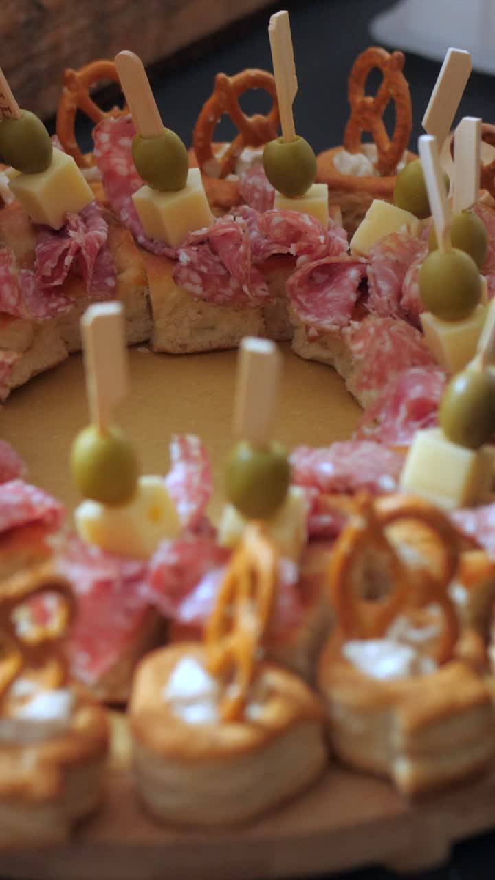 Plato de embutidos, primer plano de pan con salami, aceitunas y queso, cámara lenta vertical.