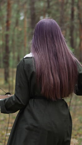 chica adolescente con ballesta camina para cazar en el bosque salvaje vista trasera. vieja arma para ataque y defensa en la búsqueda. campamento histórico para niños