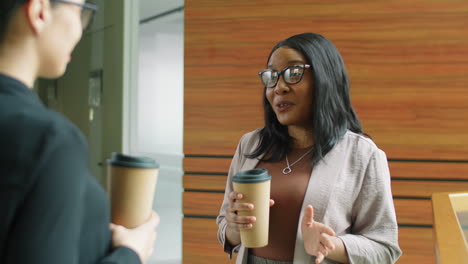 black businesswoman holding coffee and talking with colleague