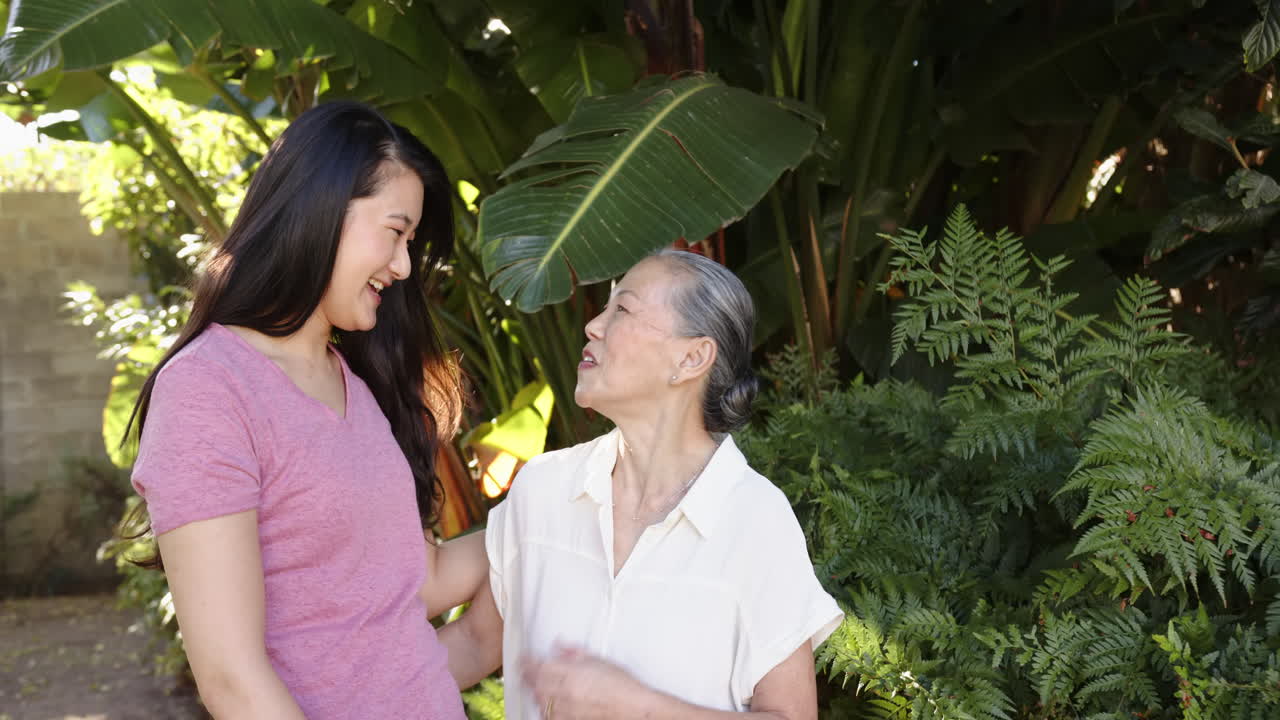 Smiling asian grandmother and granddaughter bonding together in lush garden