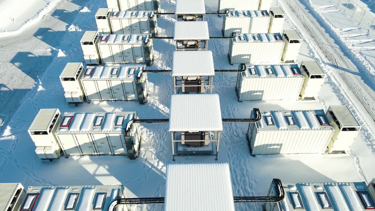 Hovering drone shot above snow covered 100MW battery storage containers in Kiisa, Estonia slowly tilting up to reveal modular grid infrastructure in winter